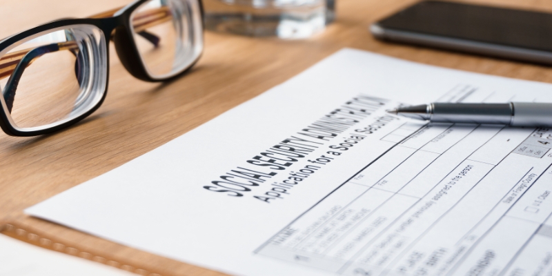 A printable Form SS-5 is laying on the table with a pen and glasses